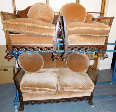 An early 20thC mahogany bergere suite, comprising two seater sofa, with cane filled arms and upholstered back and seat, with pink velvet fringed cushions, with a pierced apron scroll cast feet, and two matching armchairs, the sofa 136cm wide. - 3