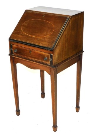 An Edwardian mahogany and boxwood strung bureau on stand, of narrow proportions, the fall flap opening to reveal three recesses and one short drawer, over one long frieze drawer, flanked by pull out stays, raised on tapering square legs and spade feet, 92