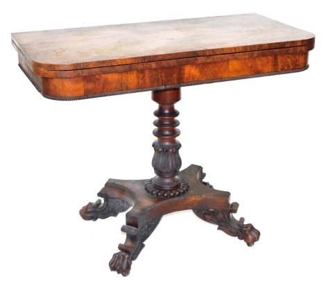 A Regency rosewood fold over tea table, raised on a turned and lappet carved column, above a quatrefoil base and foliate carved scroll feet terminating in lion's paws, on castors, 73cm high, 91.5cm wide, 45.5cm deep.