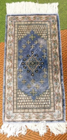 A Turkish silk rug, decorated with a central medallion surrounded by geometric design borders, against a blue ground, 93cm x 51cm.