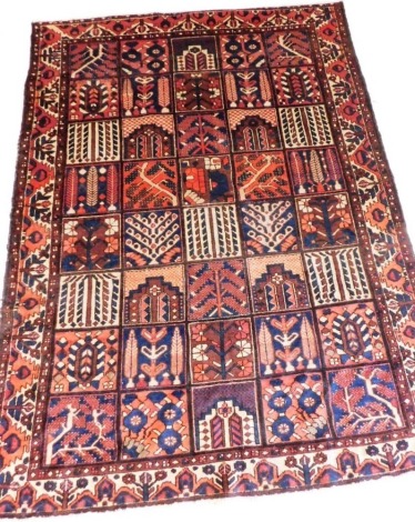 A Persian Bakhtiar red ground rug, the forty square field decorated with trees, blossom and other motifs, within a repeating floral border, 285cm x 208cm.