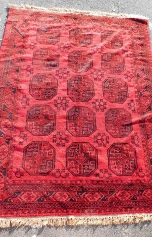 An Afghan red ground rug, decorated with fifteen octagonal medallions, interspersed with floral motifs, within a repeating floral border, 280cm x 200cm.