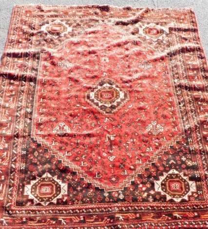 A Qashqai red ground rug, decorated with a central medallion, trees, animals, flowers and birds, the outer ground with four further medallions, and various symbols, within repeating floral borders, 268cm x 216cm.