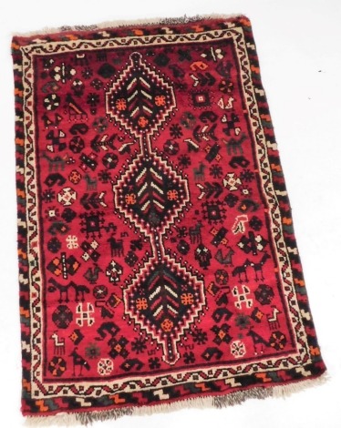 A Persian Qashqai red ground rug, decorated with three central medallions against a field with animals, birds, trees and other motifs, within repeating borders, 144cm x 98cm.