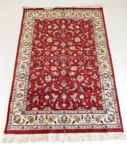 A Kerman red ground rug, the central field decorated with scrolling flowers and leaves, within repeating floral borders, 176cm x 121cm.