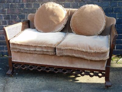 An early 20thC mahogany bergere suite, comprising two seater sofa, with cane filled arms and upholstered back and seat, with pink velvet fringed cushions, with a pierced apron scroll cast feet, and two matching armchairs, the sofa 136cm wide. - 2