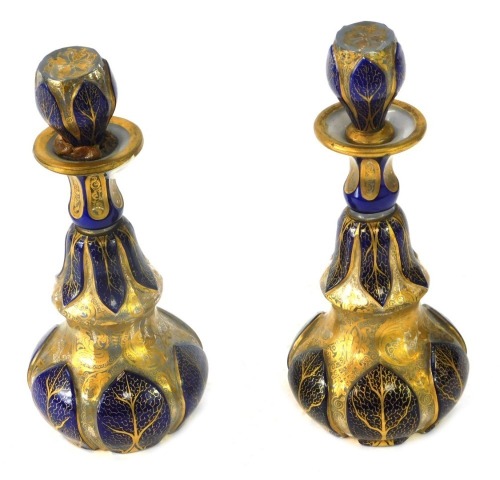 A pair of Bohemian bottles glass decanters and stoppers, each of shaped design, with royal blue painted panels and gilt scroll and vine decoration, bearing signature to underside, 19cm high, (2, AF).