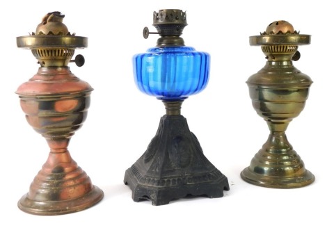 Three oil lamps, comprising Victorian cast iron oil lamp with blue glass reservoir, 30cm high, and a pair of brass effect examples, 29cm high, (AF).