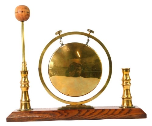 An early 20thC table top brass gong, the central gong on a stepped support, with two candlestick ends, on an oak base, with beater, 20cm high, 28cm wide, 5cm deep.