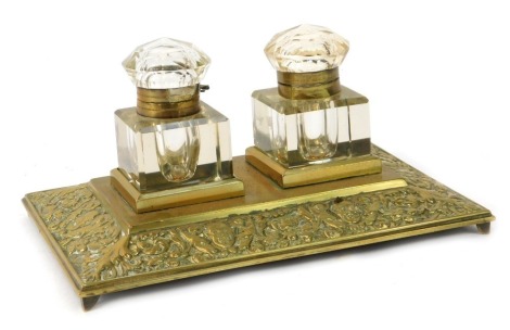 A continental brass desk stand, the central rectangular panel, with two cut glass inkwells, with scroll and foliate design order, on four cap feet, 12cm high, 22cm wide, 14cm deep.