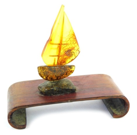 An amber ship ornament, the ship comprised of amber pieces on a stained teak base, 8cm high.