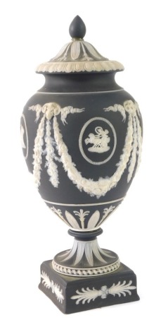 A Wedgwood black basalt ware urn and cover, with Rams head and floral swags, with chariot rider, 21cm high.