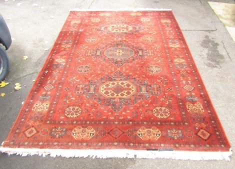 An Afghan rug, burnt orange ground with medallions and tassels, 352cm x 248cm.