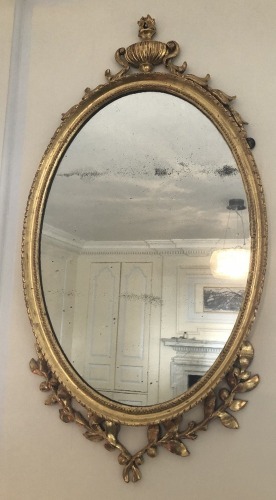 An early 19thC oval giltwood wall mirror, with Neo Classical urn and bell husk decoration, 97cm high.