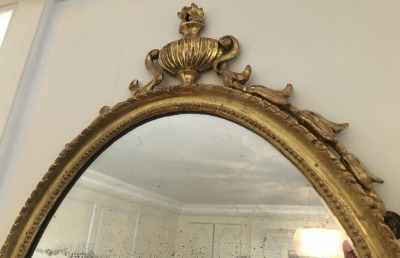 An early 19thC oval giltwood wall mirror, with Neo Classical urn and bell husk decoration, 97cm high. - 2