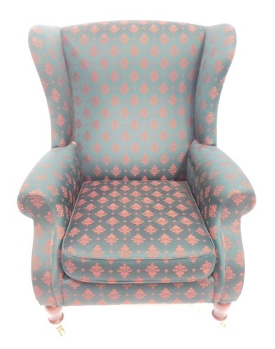 A Parker Knoll wingback armchair, upholstered in green patterned fabric on turned legs.