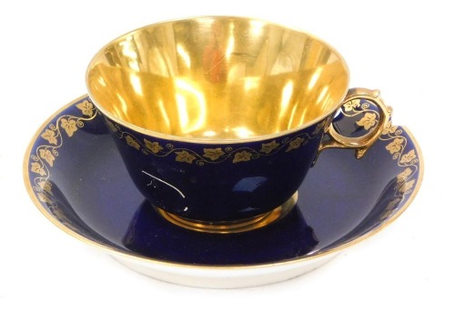 A 20thC Sevres style cup and saucer, on a cobalt blue glaze, with gilt vine detail and Napoleon crest, orange stamp to underside, stamped S57, the cup 5cm high, the saucer 14cm diameter.