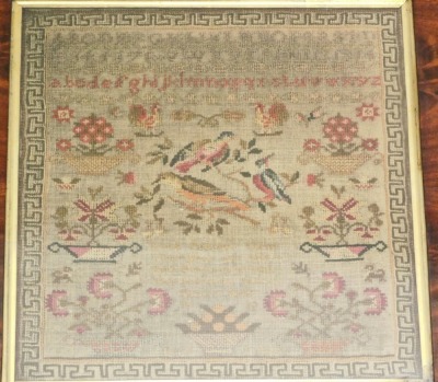 An early Victorian alphabetic pictorial and motto sampler, by Betsy Balls aged eleven years dated 1838, decorated with vases of flowers and birds, with a Greek key border with a flamed mahogany and inlaid frame, the frame 45cm x 44cm.