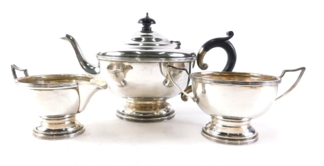 A George V silver three piece tea service, comprising teapot with ebonised knop and thumb mould handle on circular foot, 14cm high, milk jug and two handled sugar bowl, Birmingham 1931, 21oz all in.