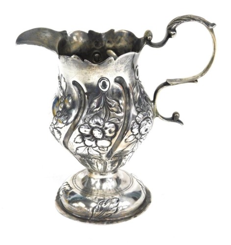 A George III cream jug, helmet shaped with S scroll handle with repousse decorated body and circular weighted foot, marks rubbed, 11cm high, 4.7oz all in.