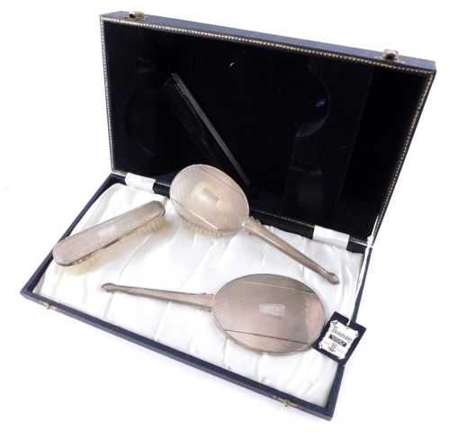 An Elizabeth II four piece dressing table set, by Broadway and Co, engine turned with vacant cartouche, to include hairbrush, 23cm long, etc., Birmingham 1961 marked Sterling. (a quantity, cased)