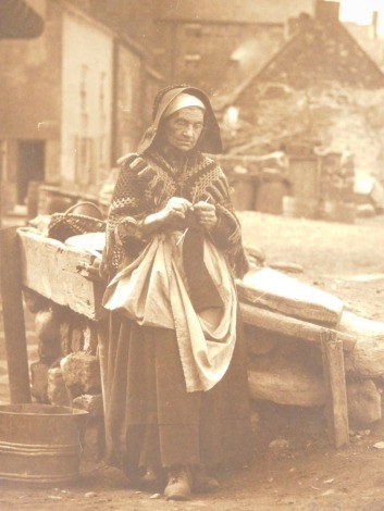 Francis (Frank) Meadow Sutcliffe (1853-1941). Elderly lady mending sails before houses, gelatin carbon print, signed, 29cm x 25cm.