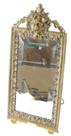 A late 19thC Continental brass dressing mirror, the frame cast with a central mask to the crest, and with foliate and beaded boarders, surrounding a bevelled plate with strut support, 48cm high, 22cm wide.