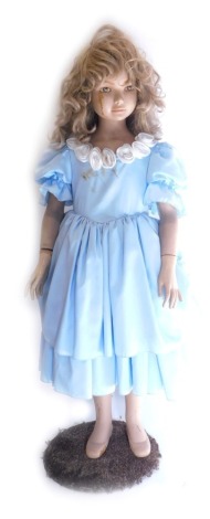 A freestanding doll figure of a girl, wearing blue dress with removable hair, on shaped base, 127cm high.