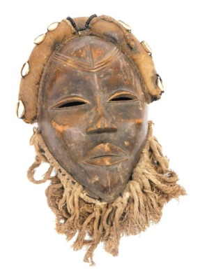 An African tribal Dan wall mask, with shell decoration to the hair and rope to the lower section, 24cm high.