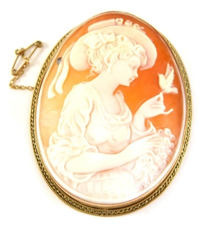 A 19thC oval shell cameo brooch, depicting a maiden with bird, in a yellow metal frame stamped 9kt with single pin back and safety chain, 7cm x 5.5cm, 25.9g all in.