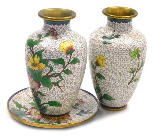 Three items of Chinese cloisonne, comprising a pair of vases and a plate, each decorated with flowers and birds on a white ground, vases 20.5cm high, plate 18cm diameter.