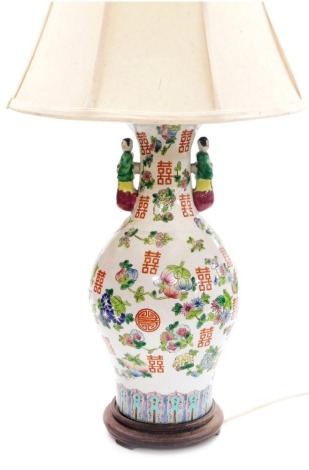 A late 20thC Chinese famile rose porcelain table lamp, of twin figural handle baluster form, decorated with peaches, vector symbols, convolvulus and other flowers, raised on a circular wooden base, with shade, vase 42.5cm high.