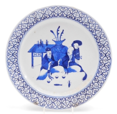 A 19thC Qing dynasty blue and white plate, decorated centrally with scholars in front of a large vase and table, within a repeating arabesque border, 25cm wide.