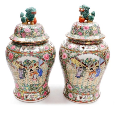 A pair of late 20thC Cantonese famille rose porcelain vases and covers, of baluster form, the covers with lion dog finials, decorated with reserves of figures in a garden, butterflies and flowers, against a gilt ground decorated with flowers, scrolls and 