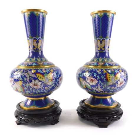 A pair of late Chinese cloisonne vases, each decorated with butterflies, flowers, etc., unmarked, hardwood bases, the vases 26cm high.