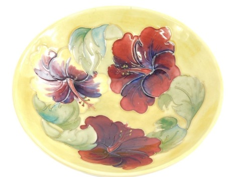 A Moorcroft Pottery shallow bowl, decorated with deep red and purple flowers and leaves, on a yellow ground with green underside, paper label to underside, 18cm diameter.