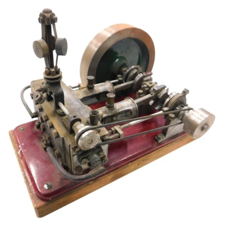 A mid 20thC tabletop engine, set with pistons and large cog, on red metal stand and wooden plinth base, 23cm wide.