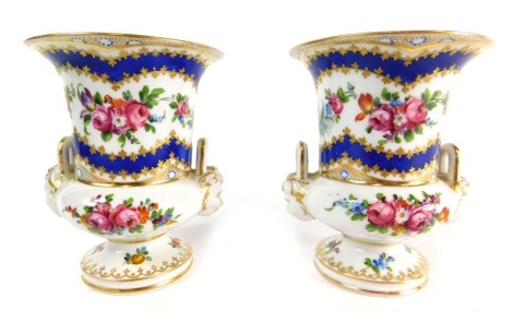 A pair of Continental porcelain urn vases, each delicately hand painted with floral garlands with gilt highlights and a blue and white ground, with mask handles on circular feet, blue script marks beneath, 12cm high.