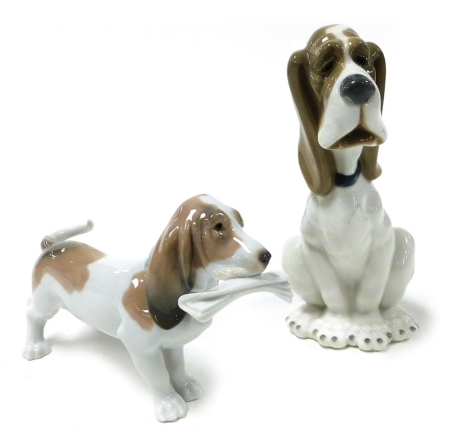 A Lladro Porcelain figure of a Basset Hound, modelled standing with a newspaper in its mouth, together with a Nao Porcelain figure of a seated Basset Hound. (2)