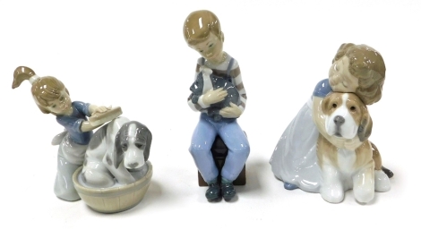 A Lladro Porcelain figure of a girl kneeling washing her dog in a tub, and two Nao figures, one of a boy seated with a puppy, a bandage around its head, the other of a girl embracing a dog. (3)