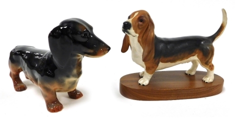 A Beswick matt pottery figure of a Basset Hound, raised on an oval wooden base, and a gloss figure of a Dachshund. (2)