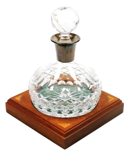 A cut glass decanter and stopper, with a silver collar, Birmingham 1987, and a mahogany stand with quarter sunburst paterae inlay.