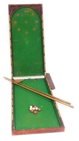 An early 20thC stained mahogany table top bagatelle, with a green baize interior, 123cm high, 115cm wide open, together with a pair of cues and balls.