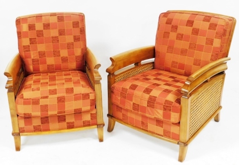 A pair of pale beech framed and cane armchairs, with red chequered loose cushions, raised on outswept feet, each 65cm wide. The upholstery in this lot does not comply with the 1988 (Fire & Fire Furnishing) Regulations, unless sold to a known exporter or u