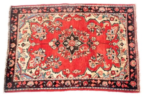 A Hamadan red ground rug, decorated with a central floral medallion, within a field of further flowers, within a repeating floral border, 200cm x 137cm.