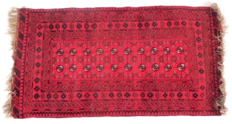 An Afghan Turkoman red ground rug, decorated with twenty guls, within repeating floral and geometric borders, 180cm x 102cm.