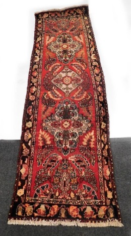 A Hamadan red ground runner, decorated with three central floral medallions, further flowers and leaves within a repeating border, 316cm x 94cm.