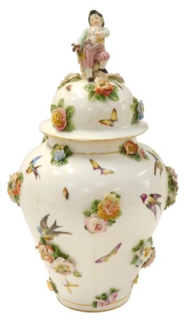 A late 19thC German porcelain jar and cover, of baluster form, the lid with figural boy finial, painted with birds, insects and butterflies, interspersed with floral encrustations, gilt heightened, pseudo blue crossed swords mark, 45cm high. (AF)