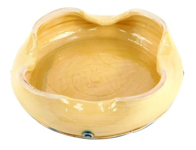 An Fenella Mallalieu studio pottery ash tray, with four point flared rim, applied green circular painted detail, on a striped foot, bearing signature, 17cm diameter.