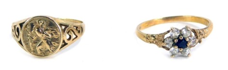 Two 9ct gold dress rings, comprising a St Christopher dress ring, with scroll design shoulders, size K½, and a CZ and blue paste stone set cluster ring, yellow metal unmarked, size L½, 3.1g all. (2)